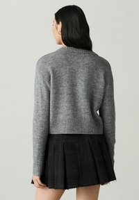 Gray cropped sweater made of textured knit fabric, featuring a ribbed hem and long sleeves, paired with a black pleated skirt.