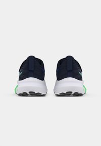 Mørkeblå treningssko med en teksturert overdel, hvit mellomsole og grønne detaljer på hælen. Svart gummisåle med mønster.