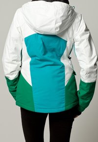 Giacca con una parte superiore bianca, un pannello centrale turchese vivace e una parte inferiore verde scuro. Ha un cappuccio e una vita regolabile.