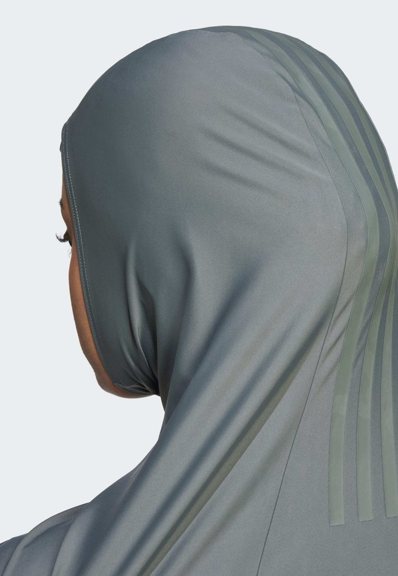 Person, der einen eng anliegenden grauen Kapuzenpullover mit drei vertikalen Streifen auf der Rückseite trägt, seitlich und von hinten gezeigt.