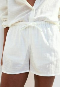 Pantaloni corti bianchi in lino con una vita elastica e chiusura con coulisse. Il tessuto presenta un aspetto leggermente testurizzato e leggero.