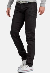 Jean skinny noir, en mélange de coton, coupe slim, design à cinq poches, accents de couture subtils, portés avec des baskets blanches.