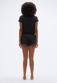 Μαύρο τοπ με κοντά μανίκια και στρογγυλή λαιμόκοψη, συνδυασμένο με μαύρα σορτς με ελαστική μέση, απεικονιζόμενο από πίσω σε ανοιχτό φόντο.