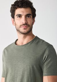 Olijfgroen crew neck T-shirt, korte mouwen, gemaakt van gestructureerde katoen, met een relaxte pasvorm en subtiele stikseldetails.