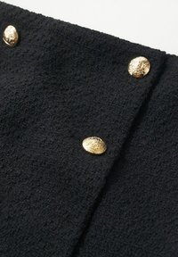 Tissu noir texturé avec trois boutons dorés brillants, chacun présentant un emblème de lion en relief, disposés en diagonale.