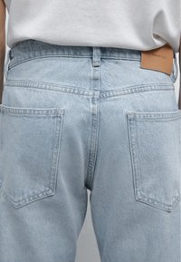 Light blue denim jeans with a straight cut, featuring two back pockets and a tan leather label at the waistband embossed with "Massimo Dutti."