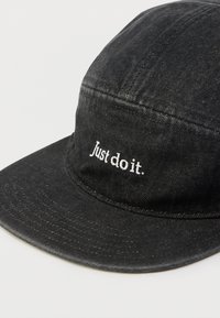 Boné de algodão preto com aba reta e texto bordado "Just do it." na frente. Apresenta um tecido texturizado e design minimalista.