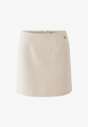 Jupe mini en tweed beige texturé avec un petit emblème rond doré près de la taille et une fermeture éclair au dos.