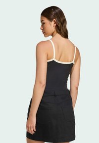 Zwarte tanktop met crèmekleurige rand en verstelbare bandjes, gecombineerd met een zwarte denim rok met achterzakken en een aansluitende taille.