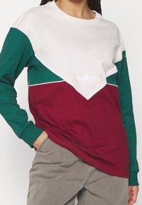 Långärmad sweatshirt med en färgblockdesign i vitt, grönt och bordeaux. Inkluderar en liten vit logotyp på bröstet. Tillverkad av bomull.