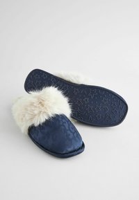 Mørkeblå hjemmesko med faux fur-trim, der har et tekstureret overmateriale med et subtilt mønster og en gummisål med mønster af stjerner.