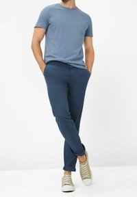 Niebieski t-shirt z okrągłym dekoltem, połączony z granatowymi, dopasowanymi spodniami o wąskim kroju, z podwiniętymi mankietami oraz beżowymi trampkami na sznurowadła. Minimalistyczny design, gładka faktura.