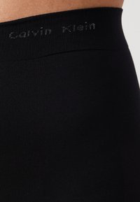 Černé legíny Calvin Klein s žebrovaným pasem, na kterém je ve šedém písmu vyvedena značka. Hladká textura, těsný střih.