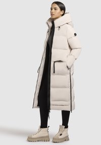 Beige puffer coat with a high collar, black zipper, and side pockets. Paired with light beige lace-up boots featuring a thick sole.