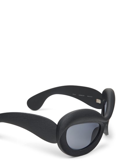 Black sunglasses with wide lenses, textured frames, and curved arms. The lenses are slightly tinted, complementing the bold, unique design.