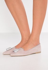 Lichtroze suède ballet flats met een spitse neus en zilveren kwastjesdetail aan de voorkant, met een lage hak en een gladde textuur.