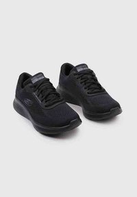 Zapatos deportivos negros fabricados con malla y materiales sintéticos, cuentan con una punta redondeada, lengüeta acolchada y una suela texturizada.