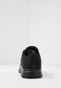 Black athletic shoe with a breathable mesh upper, textured finish, and a reinforced heel tab for easy wear. Solid rubber outsole.