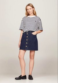 Striped white and navy T-shirt paired with a dark denim skirt featuring a front button closure and pockets, complemented by black loafers.