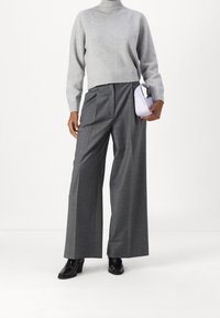 Grauer, gestrickter Rollkragenpullover kombiniert mit weiten grauen Hosen. Das Model hält eine kleine lavendelfarbene Handtasche. Schwarze Stiefeletten mit Absatz runden das Outfit ab.