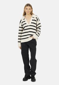 Maglione a righe nere e crema, lavorato a maglia, con scollo a V e vestibilità oversize, abbinato a jeans neri a gamba larga e scarpe nere chunky.