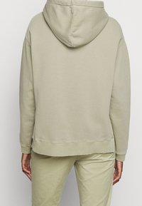 Sudadera con capucha en un tono beige suave. Presenta un dobladillo y puños acanalados. La tela parece suave y ligeramente texturada, con un ajuste relajado.