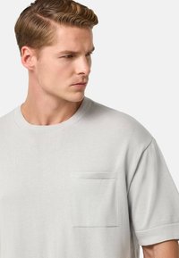 T-shirt grigio chiaro a maniche corte in tessuto morbido, con taschino sul petto. Design semplice con scollatura a girocollo e texture sottile.
