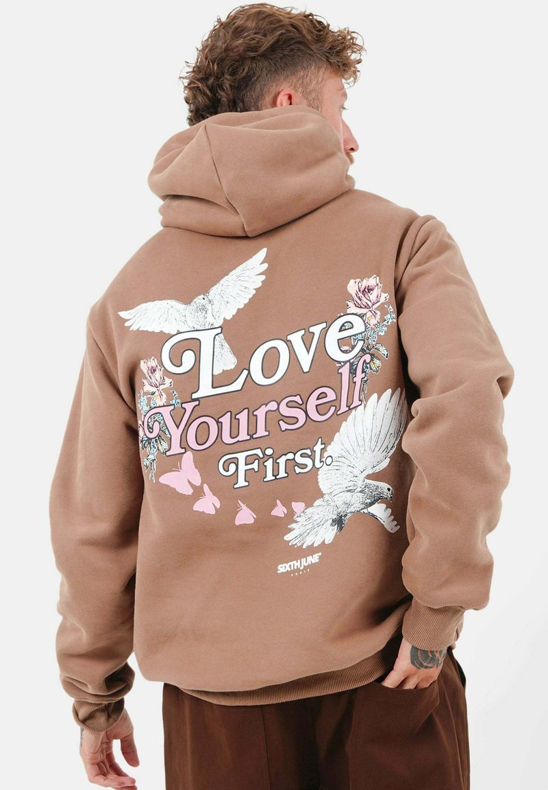 Brunt hoodie med vit och rosa texten "Älska dig själv först," med blommönster och duvor. Mjuk tygkvalitet, avslappnad passform och med huva.