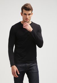 Sort langærmet t-shirt lavet af glat bomuldsstof, med rund halsudskæring og tætsiddende design, parret med mørk denimjeans.