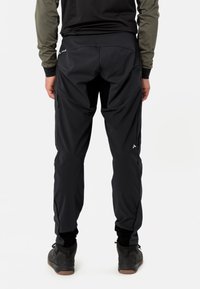 Pantalons légers noirs avec taille élastique, coupe fuselée et poches zippées. Le matériau est lisse, avec une finition mate et un branding minimal.