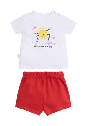 Camiseta blanca para niño pequeño con un sol sobre una patineta y pantalones cortos rojos, el texto de la camiseta dice "Aquí viene la diversión."