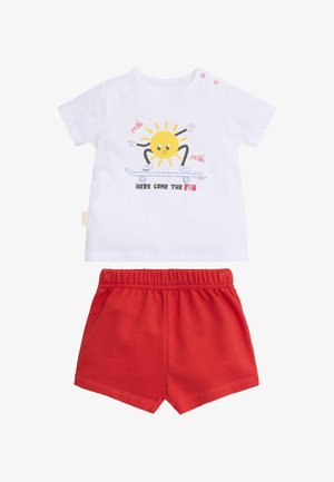 Camiseta blanca para niño pequeño con un sol sobre una patineta y pantalones cortos rojos, el texto de la camiseta dice "Aquí viene la diversión."