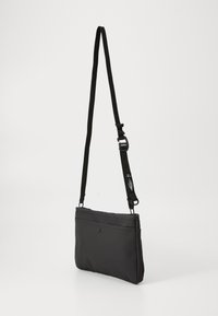 Black crossbody bag made of soft, textured material, featuring a zippered top, a front pocket, and an adjustable strap.