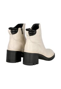 Botines de cuero beige con un tacón y detalles negros, que presentan una cremallera lateral y una suela de plataforma texturizada.