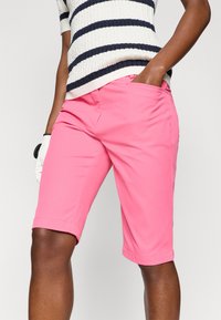 Calções rosa com corte reto, bainha dobrada e bolsos frontais. O material parece liso, com costuras mínimas e um design ajustado.