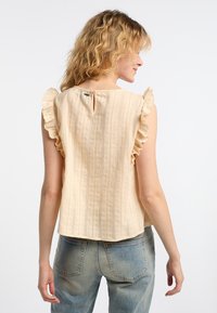 Top beige senza maniche con dettagli a volant sulle spalle, caratterizzato da sottili righe testurizzate e una chiusura a bottoni sul retro.
