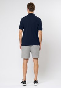 Námořní modré polo tričko s krátkými rukávy v kombinaci se šedými šortkami. Tento outfit má standardní límec a uvolněný střih, doplněný o černé tenisky.