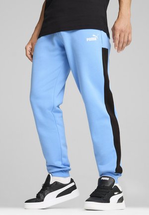 Light blue sweatpants with black side stripes, featuring a white Puma logo on the left thigh. Paired with black and white sneakers.