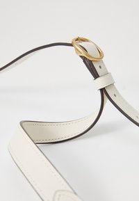 Cream leather belt with dark brown edges, featuring a gold circular buckle and a sleek, smooth texture. Adjustable with multiple holes.