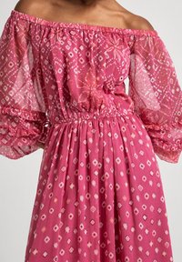 Pink, off-the-shoulder dress with sheer puff sleeves. Features an elastic waist and a pattern of white and darker pink diamond shapes.