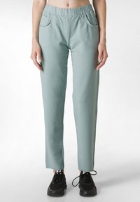 Pantalones de chándal verde claro con cintura elástica, dos bolsillos laterales y un diseño de pierna recta, combinados con zapatillas deportivas negras.