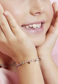 Perlenarmband mit rosa, blauen und goldenen Perlen sowie kleinen Herz-Anhängern. Nahaufnahme einer Hand, die nahe einem lächelnden Gesicht ruht.