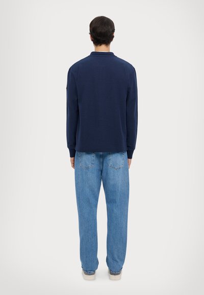 Polo a maniche lunghe navy con colletto, abbinato a jeans blu chiaro a vestibilità ampia e sneaker color avorio, visto da dietro.