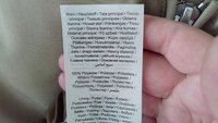 Étiquette comportant plusieurs langues, indiquant "Matériau principal : 100 % Polyester," ainsi que des détails sur l'entretien et la composition. Tissu lisse de couleur claire.