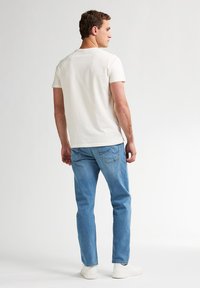 Camiseta de algodón crema claro combinada con jeans de mezclilla azul claro y zapatillas blancas; costuras visibles y un ajuste casual.