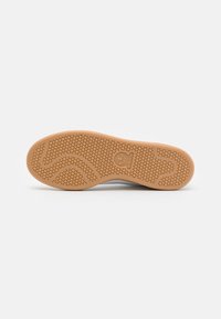 Suela de zapatilla de goma con un patrón de panal y un logo central. Color marrón claro con líneas curvas para tracción y agarre.