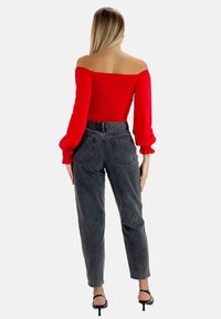 Top rojo sin hombros con diseño fruncido; mangas largas abullonadas. Combinado con jeans de mezclilla negros de tiro alto, ajuste casual. Tacones negros con tiras.
