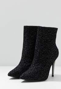Stivali neri alla caviglia realizzati in materiale testurizzato con un sottile motivo a stampa leopardata. Presentano una punta appuntita e un alto tacco a stiletto metallico.