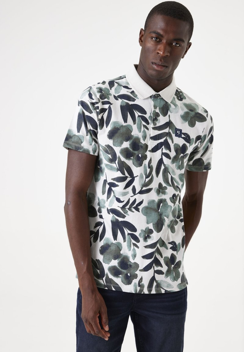 Korte mouw polo shirt van lichtgewicht stof met groene en marineblauwe bloemenpatronen op een witte achtergrond. Klassieke kraag met drie knopen.