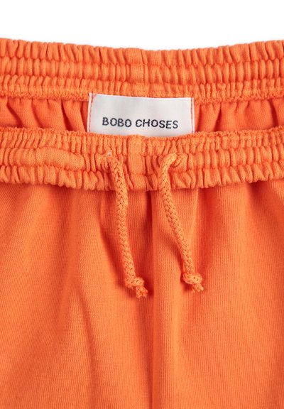 Oranžové bavlnené šortky s elastickým pásom. Obsahujú šnúrku na stiahnutie a štítok s nápisom "BOBO CHOSES" v čiernom písmene. Hladká textúra.